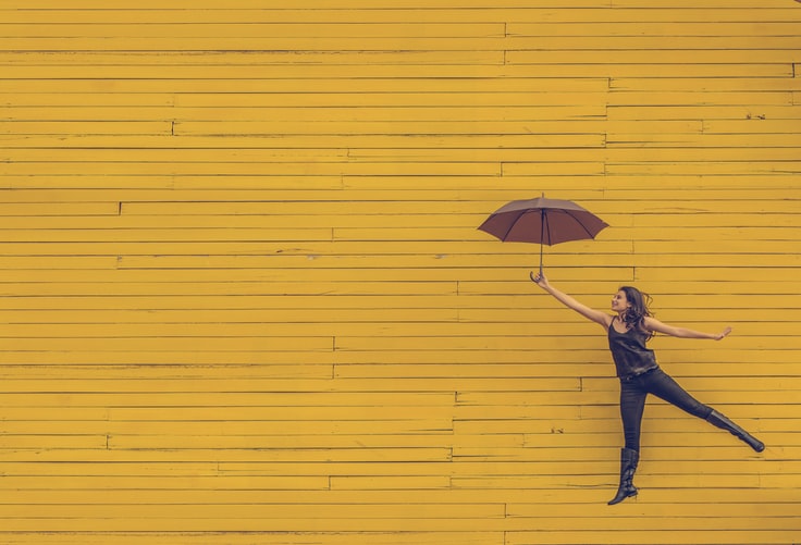 Person with umbrella floating against yellow wooden wall background